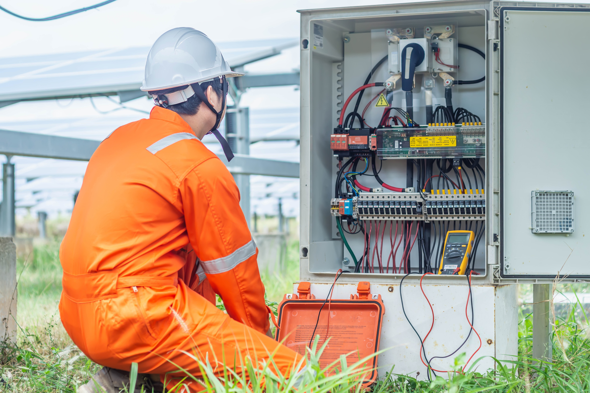 Elektryk w kasku i odzieży ochronnej sprawdzający instalację elektryczną multimetrem przy rozdzielni